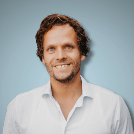 Bastian Hiller Teejit Portrait stehend vor hellblauem Hintergrund