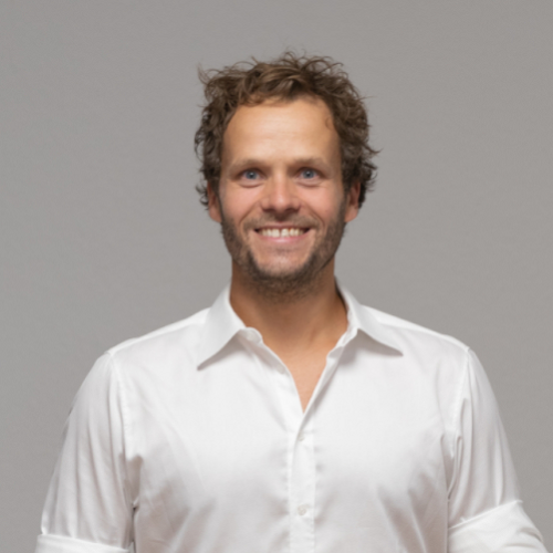 Bastian Hiller Portrait stehend vor hellblauem Hintergrund