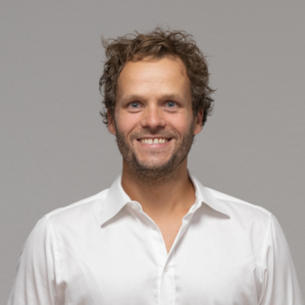 Bastian Hiller Portrait stehend vor hellblauem Hintergrund